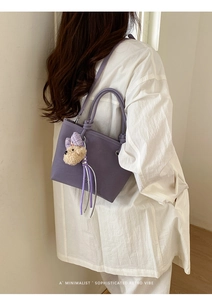 Chic purple bucket bag with plush bear charm and tassels on a model shoulder