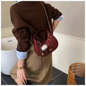 Close-up of wine red quilted crescent bag with gold chain and plush ball charm