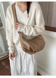 Detail view of light brown ruched leather shoulder bag worn by model with neutral outfit