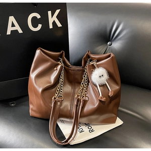 Close-up of dark brown leather tote bag with gold chain and plush doll pendant detail