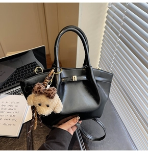Détail du sac à main en cuir noir brillant avec fermoir métallique et breloque