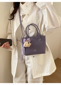 Detail of purple bucket bag with woven handle, white lettering and cute bear charm accessory