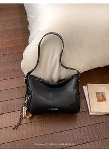 Detail of black leather crescent tote bag with white contrast stitching and tassel charm