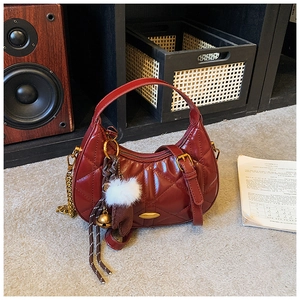 Detail of a dark red quilted half-moon handbag with gold chain and plush keychain