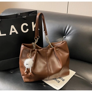 Detail of a brown leather tote with gold chain strap and a plush monster charm on a sofa