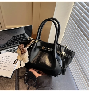 Détail d'un sac à main noir brillant avec un pendentif chiot en peluche et un nœud léopard