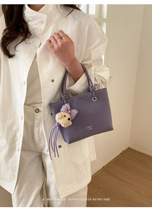 Detail of purple matte leather bucket bag with teddy bear charm and white printed logo