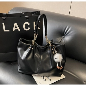 Detail view of black faux leather tote bag with gold chain strap and plush monster charm