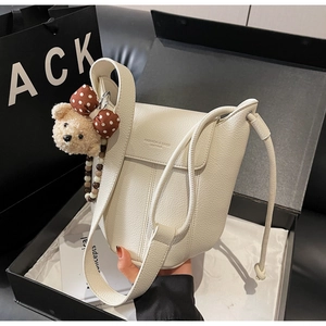 Close-up of creamy white lychee grain leather bucket bag with cute bear charm in a gift box