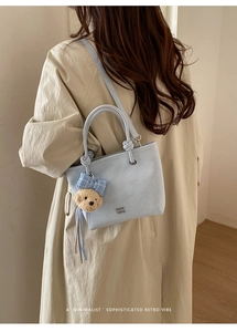 Detail of light blue bucket bag with knotted handle and cute plush bear charm on side