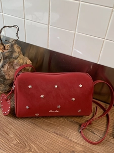 Sac polochon rouge foncé avec clous étoiles et pendentif cœur sur table en bois