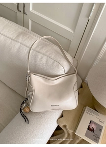 Detail view of a cream leather crescent bag with brand embossing and decorative knot charm