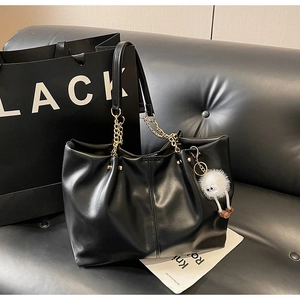 Macro shot of large black tote bag with glossy leather texture and golden chain strap
