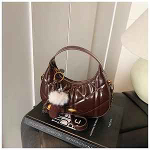 Close-up of brown quilted patent leather crescent bag with plush ball and gold hardware