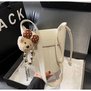 Close-up of white lychee leather bucket bag with magnetic clasp and cute teddy bear charm