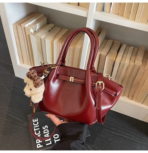 Détail d'un sac à main rouge brillant avec boucles dorées et pendentif chiot blanc