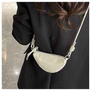 Détail d'un mini sac à bandoulière en forme de croissant crème sur une veste noire