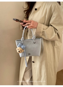 Detail of light blue bucket bag showing leather texture and cute bear charm pendant
