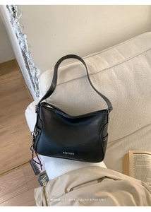 Detail of black faux leather shoulder bag with white stitching and brand logo on sofa