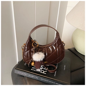 Detail of dark brown quilted crescent bag with charms on top of interior design books