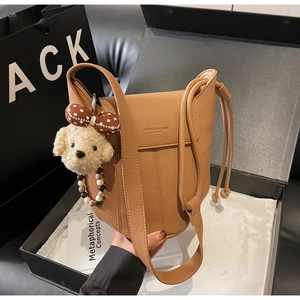 Detail view of brown lychee grain leather bucket bag with a cute plush dog charm