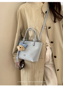 Detail of light blue bucket bag featuring a cute plush bear charm and metallic hardware