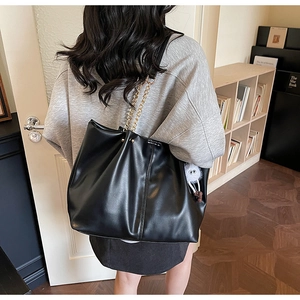 Large black tote bag with gold chain strap and plush charm shown on person