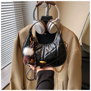 Detail of black quilted crescent bag with gold chain and plush ball charm accessory