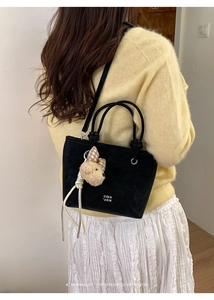Detail of black suede bucket bag with round handles and cute plush bear accessory