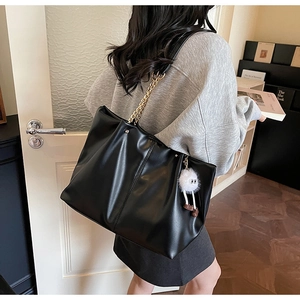 Detail of black pleated tote bag with golden chain strap and plush monster charm
