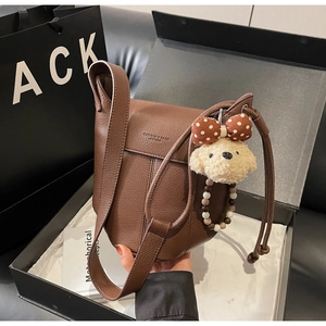 Detailed view of brown lychee grain leather crossbody bag with cute plush puppy charm