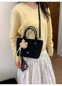 Detail of black bucket bag with plush bear charm and branding shown on model