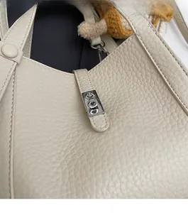 Détail du sac seau en cuir grainé beige avec fermoir rotatif en métal argenté brillant