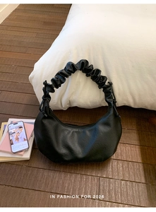 Detail of black pleated hobo bag with scrunchie strap and matte leather texture