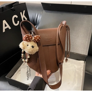 Close-up of brown textured leather shoulder bag with cute plush bear and bead charm decoration