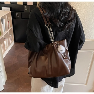 Detailed texture of dark brown faux leather tote with metal chain and pompom charm