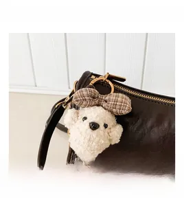 Detail of plush dog charm with plaid bow attached to a brown leather baguette bag
