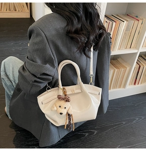 Détail d'un sac seau en cuir blanc crème avec une breloque chiot en peluche sur un blazer