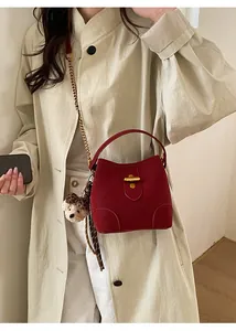Détail du sac seau rouge foncé avec fermoir doré et foulard en soie sur trench