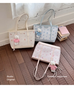 Dettaglio di tre borse tote in tela color crema, blu e rosa con ciondoli a forma di orso