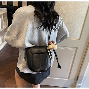 Detail of black lychee grain leather bucket bag with a cute plush animal charm