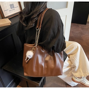 Detail of a large brown faux leather tote bag with metal chain strap and furry ball charm
