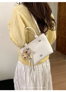 Detail of white leather bucket bag with cute teddy bear charm and brown checkered bow