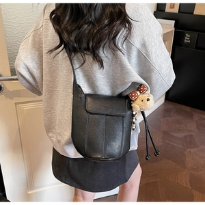Detail of black pebbled leather bucket bag on model with cute plush bear charm