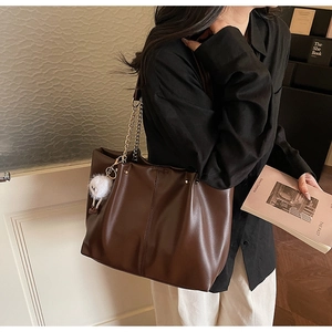 Detail of dark brown tote bag featuring fine leather texture and metal chain strap details