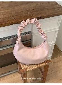 Detailed view of pink pleated crescent bag with scrunchie strap on a wooden table