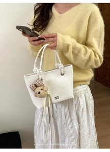 Close-up of a white bucket bag with a cute teddy bear charm and unique knotted handle detail