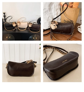 Close-up of minimalist leather baguette bag with metal chain strap and cute bear charm