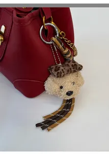 Détail d'un charme ours en peluche avec nœud léopard et franges sur un sac rouge