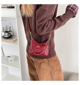 Detail of red quilted crossbody bag with gold chain and turn-lock on female model